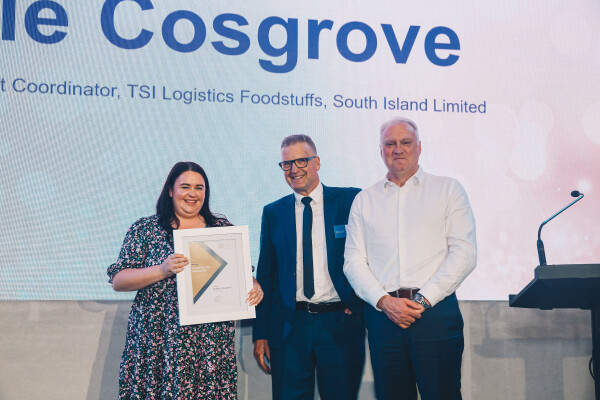  Sophie Cosgrove holds up a certificate, as she stands next to Sturrock Saunders and Andrew Body, on a stage with her name in large letters behind them.