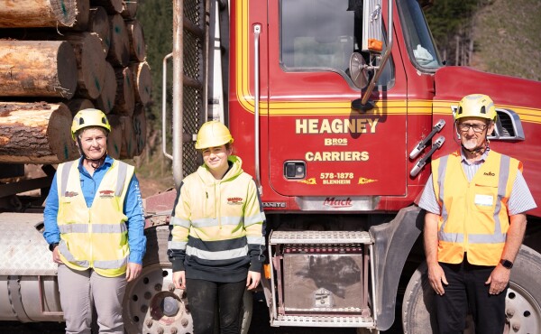 Three people standing in front of a logging truck