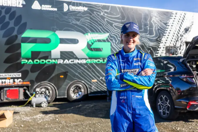 Emma Gilmour in racing kit, standing in front of Paddon Racing Group truck.