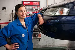 Apprentice standing in front of car, smiling