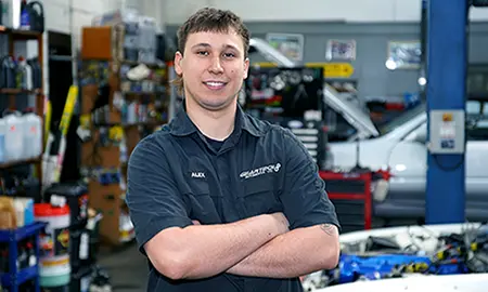Alex Parker, arms crossed, smiling in a workshop