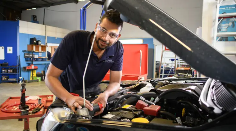 Mali Silva looking towards the camera as he works on a vehicle in an automotive workshop.